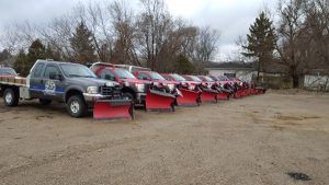 Lineup of snowplow trucks parked in an outdoor lot, showcasing Against the Elements LLC's snow removal fleet.